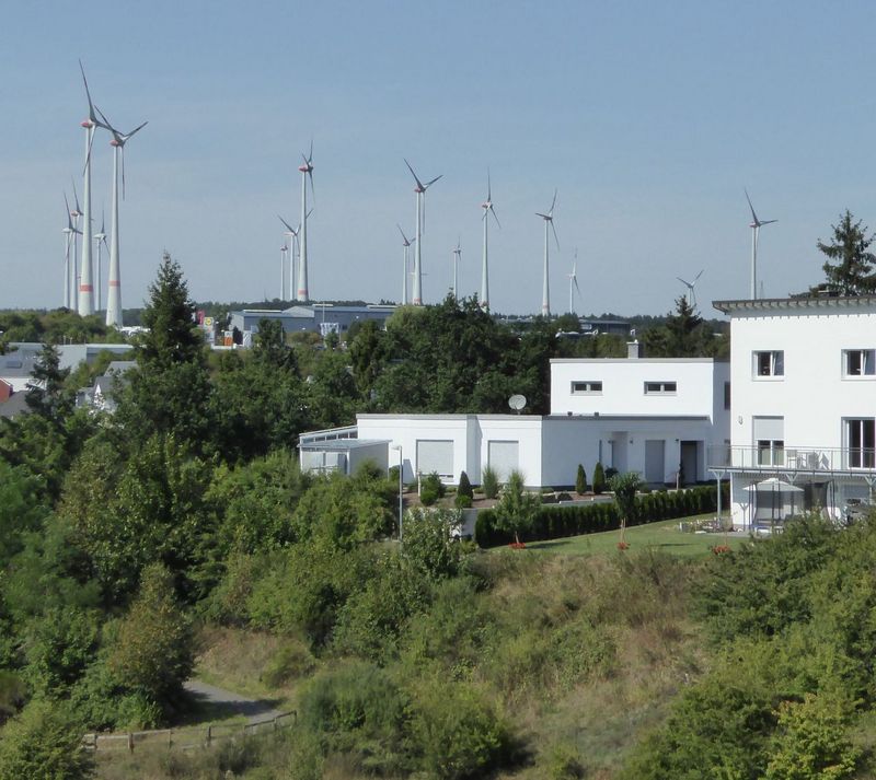 Das Bild zeigt ein Wohngebiet mit Windkraftanlagen im Hintergrund