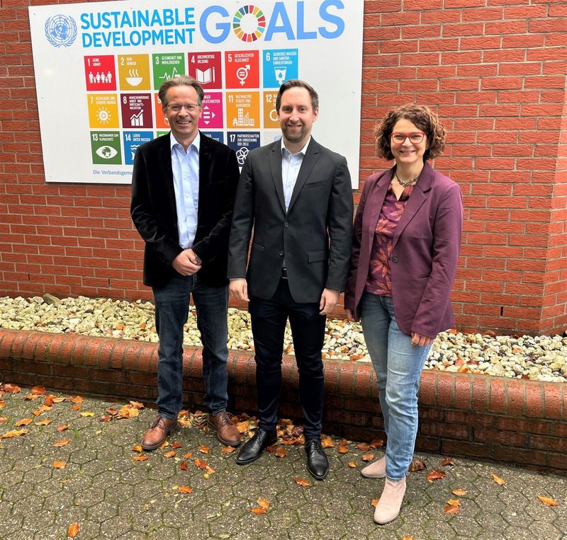 Das Bild zeigt drei Personen vor einer Tafel mit den globalen Nachhaltigkeitszielen